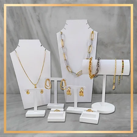 A jewelry set displayed on white mannequin stands and a cylindrical holder against a gray marble-patterned background. The set includes gold and silver chain necklaces, hoop and drop earrings, bracelets, rings, and a watch band, arranged neatly with a thin gold border around the image.